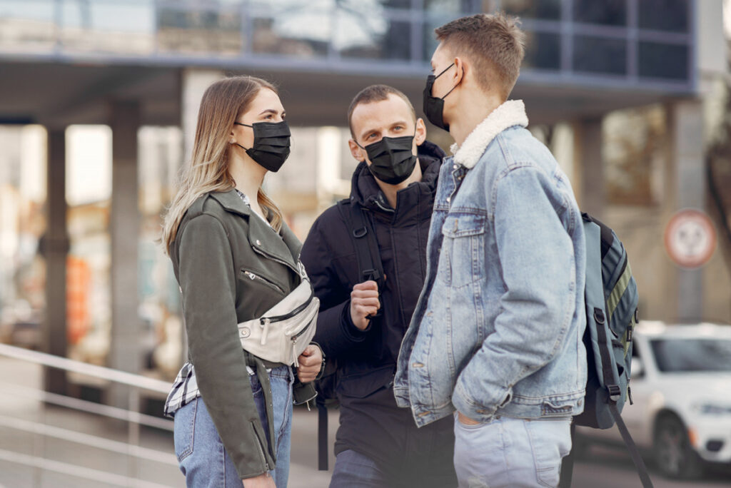 Drei junge Erwachsene mit Mund-Nasenschutz unterhalten sich im Freien.